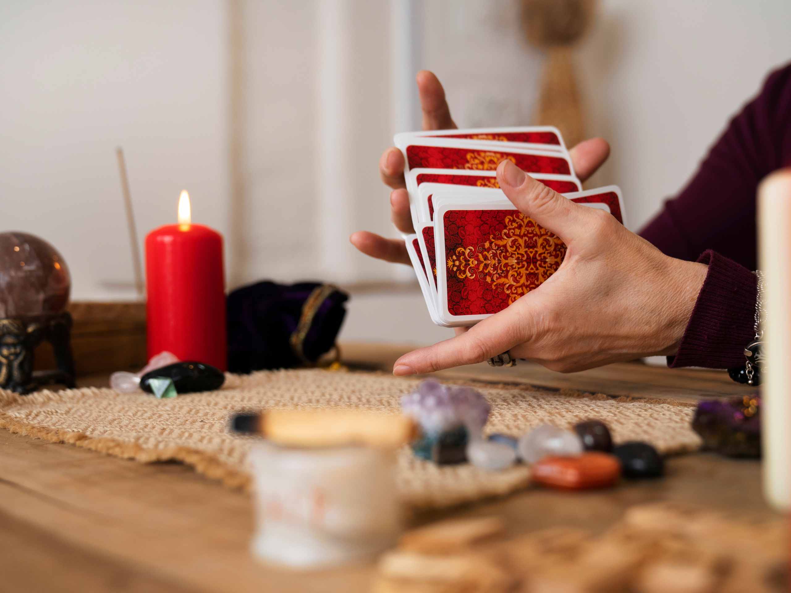 Orakelkaarten gebruiken: vrouwenhand schudt een kaartendeck, omgeven door palo santo en edelstenen